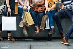 several women sitting on a wall with shopping bags and laptops in their hands,