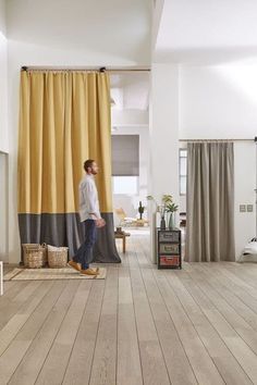 a man standing in front of a yellow curtain on top of a hard wood floor