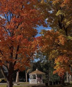 a gazebo in the middle of a park surrounded by trees with orange and yellow leaves