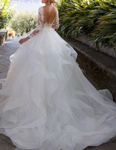 a woman in a wedding dress standing on a stone walkway near some bushes and trees