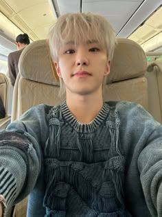 a young man sitting on an airplane with his hands in the air and looking at the camera