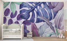 a baby's room with a wall mural featuring tropical leaves