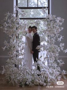 a man and woman standing in front of a window with white flowers on the floor