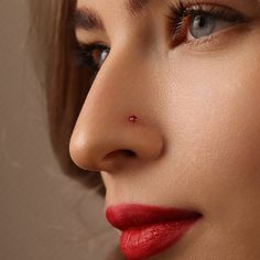 a woman with red lipstick and piercings on her nose looking off to the side