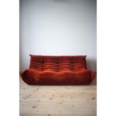 an orange couch sitting on top of a hard wood floor next to a white wall