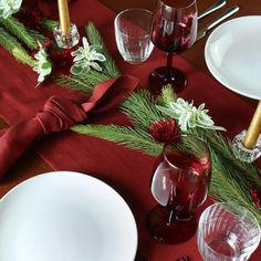 the table is set for christmas dinner with red and white dishes, silverware, and greenery