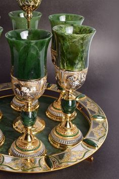 three green glass vases sitting on top of a gold platter with candlesticks