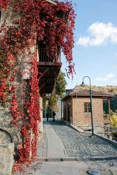 an old stone building with red vines growing on it's side and a person walking down the street