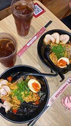 two black plates with noodles and meats on top of a table next to drinks