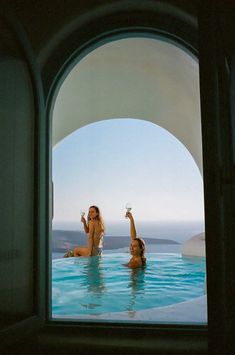 two women sitting in a swimming pool drinking wine