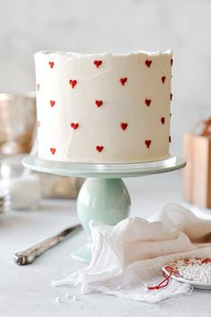 a white cake with red hearts on it sitting on a table next to silverware