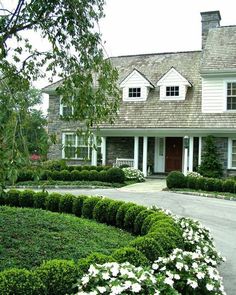 a large house with white flowers in the front yard and bushes around the driveway area