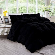 a black comforter set on a white bed in a room with large windows and plants