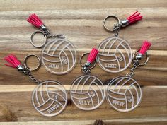 four volleyball keychains with red tassels are on a wooden surface,