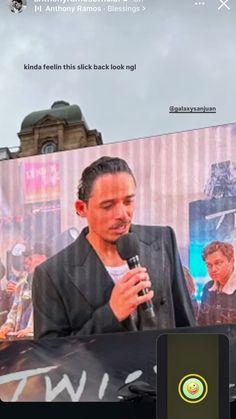 a man holding a microphone standing in front of a screen with an advertisement on it