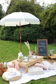 a picnic table set up with an umbrella and pillows on the grass, next to a chalkboard sign that says happy birthday mom