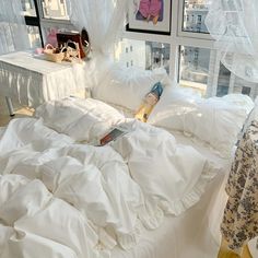 an unmade bed with white sheets and pillows in front of a window overlooking the city