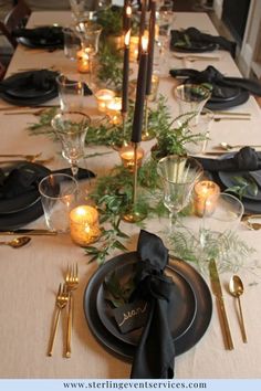 the table is set with black plates and candles