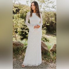 a woman wearing a white dress standing in front of some rocks and trees with her hands on her hips