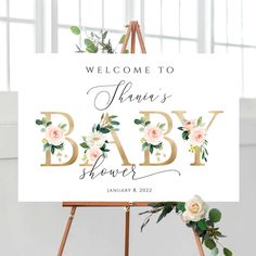 a welcome sign for a baby shower with flowers and greenery on the easel