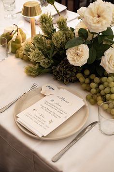 a place setting with flowers, fruit and menus on the table for an event