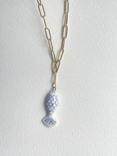 a blue and white fish necklace on a gold chain