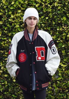 a woman standing in front of a hedge wearing a black and white jacket with red letters on it