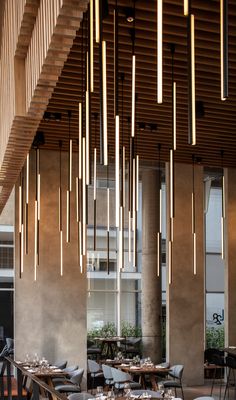 an indoor dining area with tables, chairs and lights hanging from the ceiling in front of windows