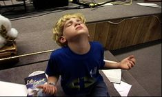 a young boy is sitting on the floor with his eyes closed and looking up at something