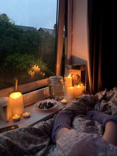 candles are lit on the window sill next to a plate of food and cupcakes