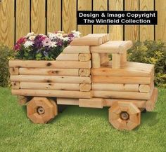 a toy truck made out of logs sitting in the grass next to a wooden fence