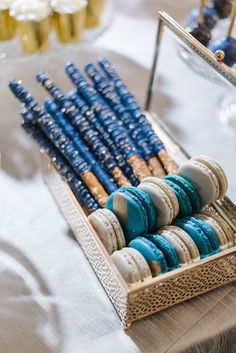 an assortment of macaroons in a tray on a table with other desserts