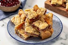 a pile of cranberry bars on a blue and white plate next to a bowl of cranberries