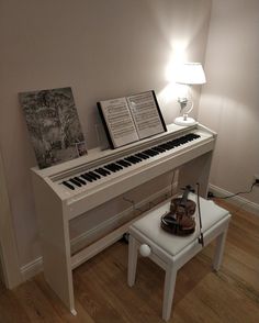 a white piano sitting on top of a hard wood floor next to a table lamp