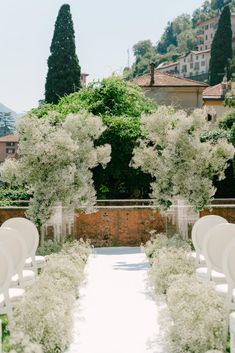 an outdoor ceremony set up with white chairs and flowers in vases on the aisle