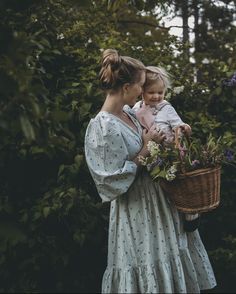 a woman holding a child in her arms while she holds a basket full of flowers