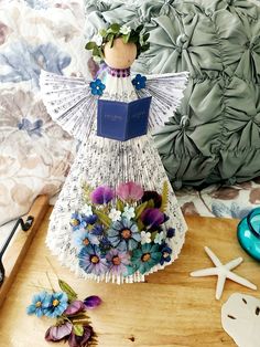 a decorative angel figurine sitting on top of a wooden table next to flowers