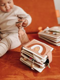 a baby sitting on top of a table next to stacks of folded books and playing with a cell phone