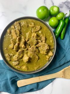 a pan filled with meat and green peppers on top of a blue towel next to a wooden spoon