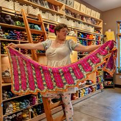 a woman standing on a ladder in front of a rack of crocheted items