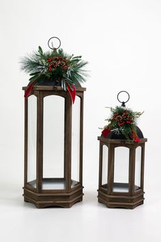 two wooden lanterns decorated with holly and pine cones, one has a red bow on the top