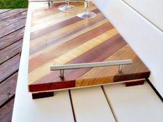 two wine glasses sitting on top of a wooden table next to a white bench and grass