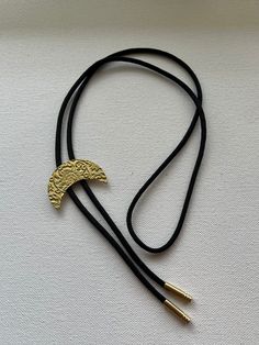 Bright yellow/gold brass crescent moon with floral pattern bolo tie necklace on black nylon cord. Brass Necklace With Adjustable Cord, Adjustable Brass Necklace With Cord, Festival Gold Jewelry With Adjustable Cord, Gold Jewelry With Sliding Knot For Festival, Festival Lariat Bolo Tie With Adjustable Length, Adjustable Crescent Brass Jewelry, Adjustable Lariat Bolo Ties For Festivals, Handmade Adjustable Bolo Ties For Festivals, Adjustable Lariat Bolo Tie For Festivals