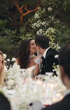 a bride and groom sharing a kiss at their wedding reception in front of white flowers