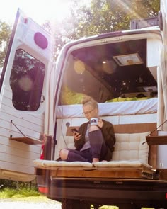 an older woman sitting on the back of a truck looking at her cell phone while holding a camera