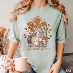 a woman is holding a cup and wearing a t - shirt with the image of beauty and the beast on it