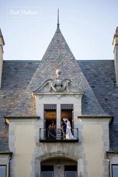 a bride and groom are standing on the balcony of their castle - like wedding venue