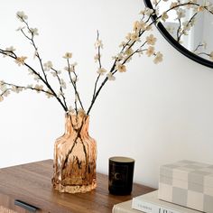 a vase with white flowers sitting on a table next to a stack of books and a mirror