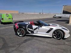 a white and black sports car parked next to a green truck in a parking lot