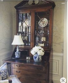 an antique china cabinet with glass doors and flowers on the top, in a living room